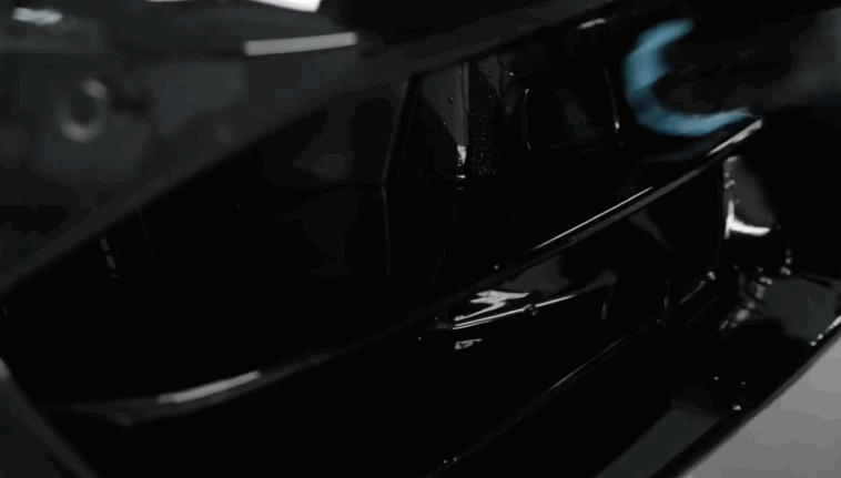 A technician uses a blue detailing cloth to carefully polish the shiny black front grille of a luxury car, emphasizing the vehicle’s high-gloss finish.