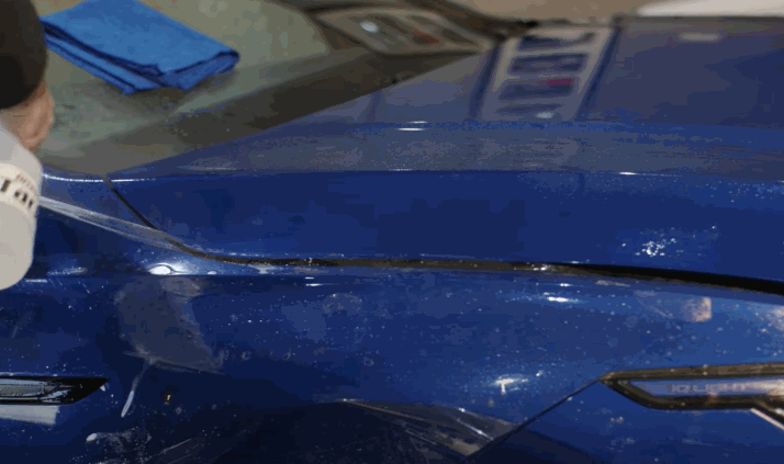 A close-up view of the PPF being peeled and adjusted on a blue vehicle’s fender during installation.